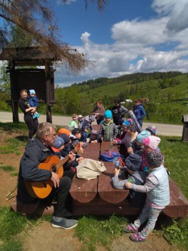 Piknik na szczycie Łapszanki. Dzieci bawią się na łące, pieką kiełbaski i śpiewają piosenki przy akompaniamencie gitary