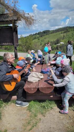 Piknik na szczycie Łapszanki. Dzieci bawią się na łące, pieką kiełbaski i śpiewają piosenki przy akompaniamencie gitary