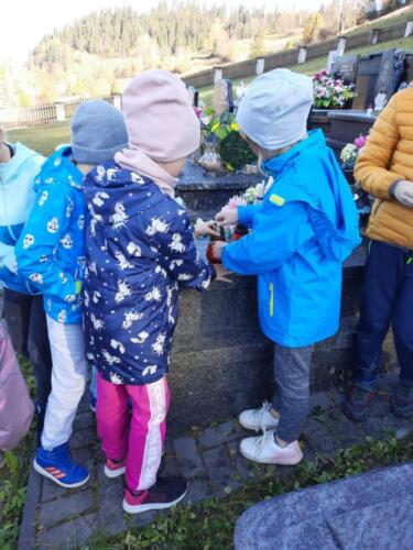 Uczniowie szkoły podczas wizyty na cmentarzu zapalają znicze.
